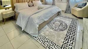A modern bedroom with a large bed, a bedside table, a chair, a decorative wall piece, and a patterned rug. - Stardust Apartments (Abuja)