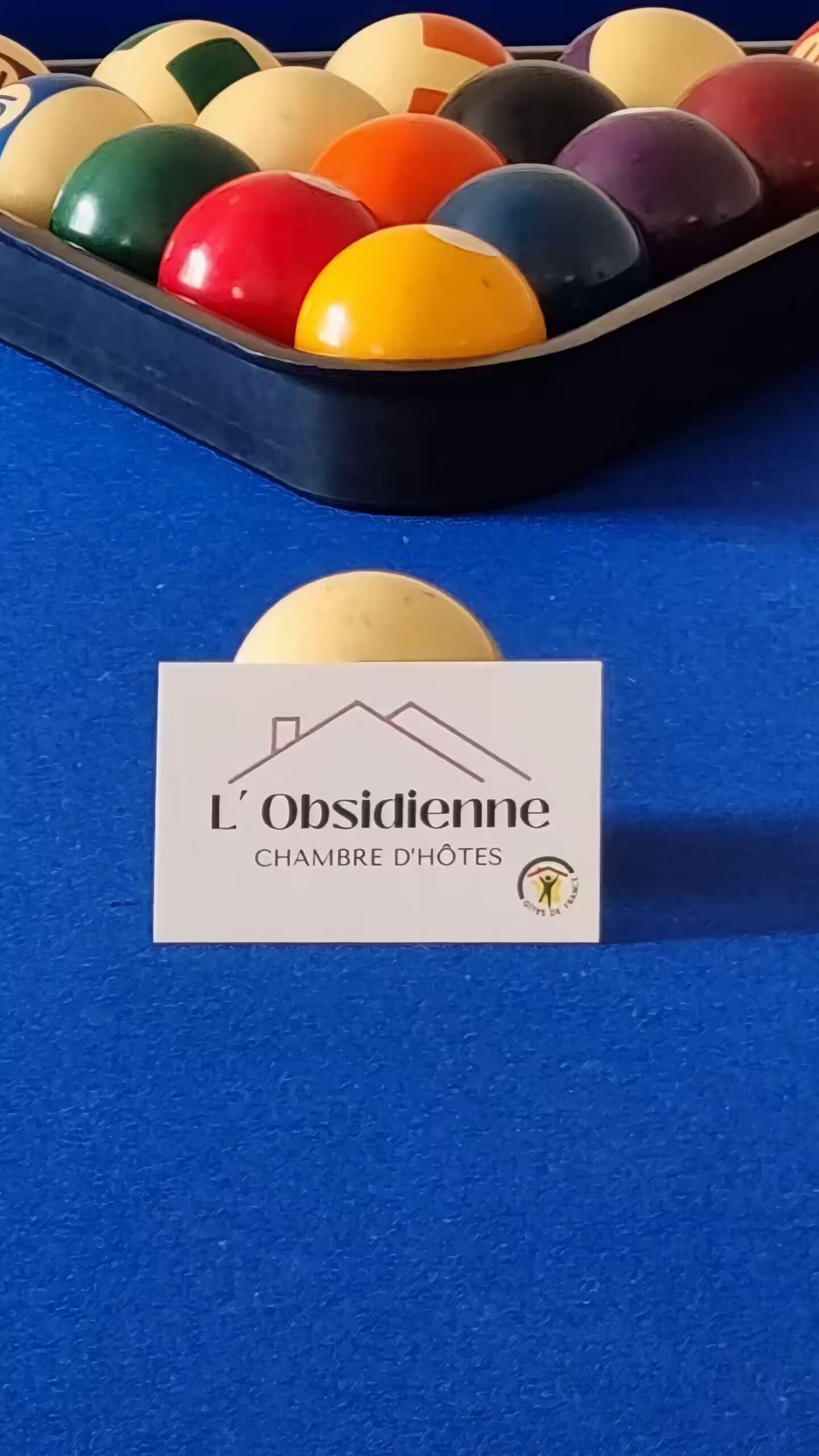 A billiards table with a variety of colored balls and a logo for 'L'Obsidienne Chambre d'Hôtes'.
