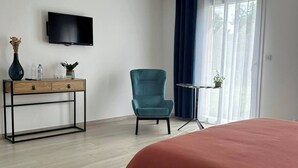 Une chambre d’hôtel avec un lit, un bureau avec une télévision, une chaise et une fenêtre avec des rideaux.