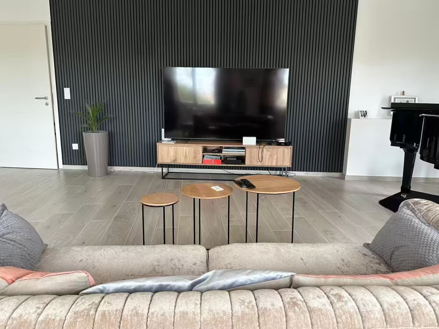 A modern living room with a large flat-screen TV, a wooden entertainment unit, and a sofa with cushions.