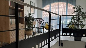 Un intérieur moderne avec une bibliothèque en bois, une rambarde noire et une vue sur l’extérieur grâce à de grandes fenêtres.