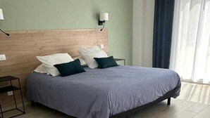 Une chambre à coucher avec un lit, une table de chevet, une lampe fixée au mur et une fenêtre avec des rideaux.