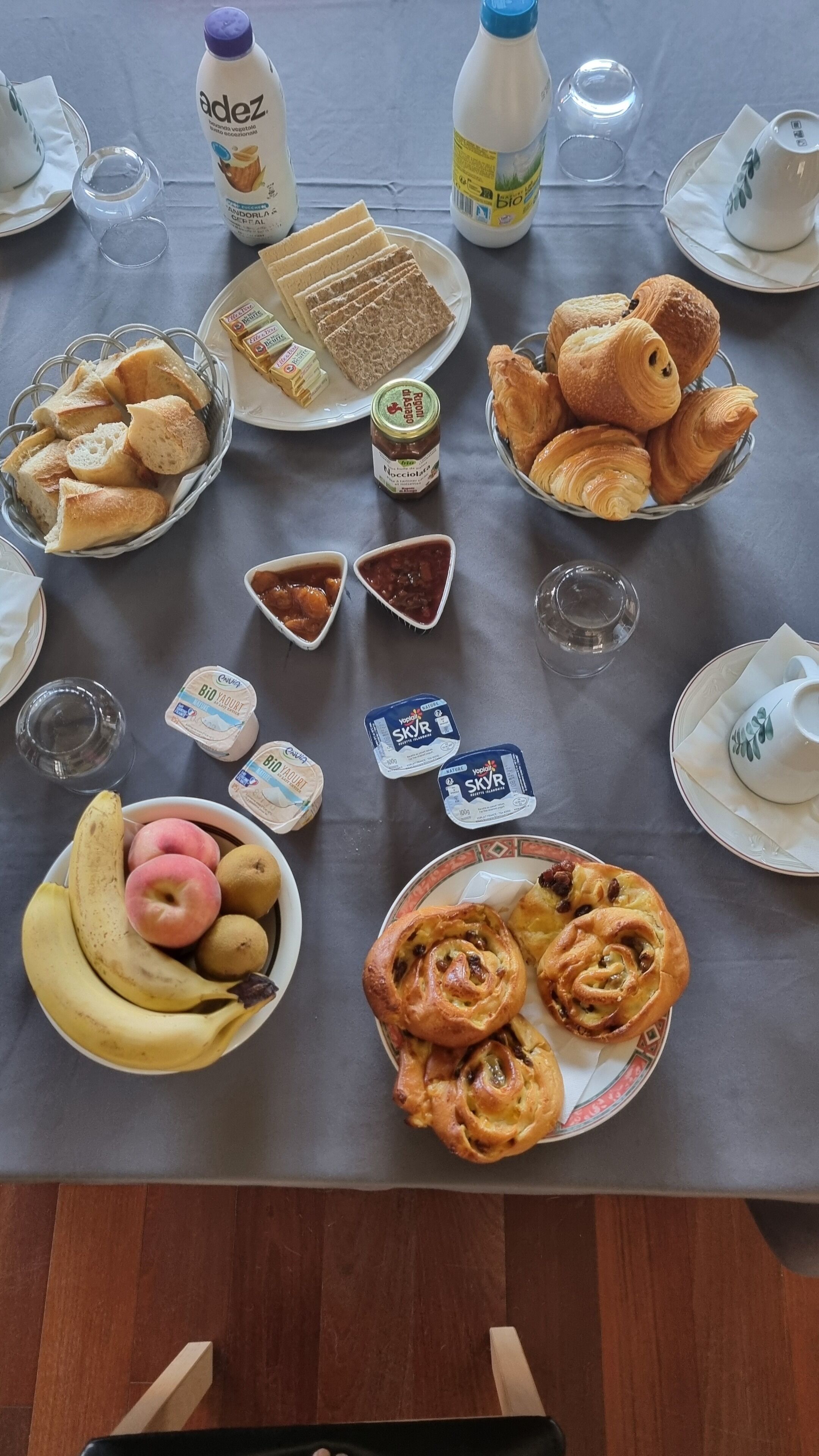 Une table de petit-déjeuner avec du pain, des viennoiseries, des fruits et du yaourt.