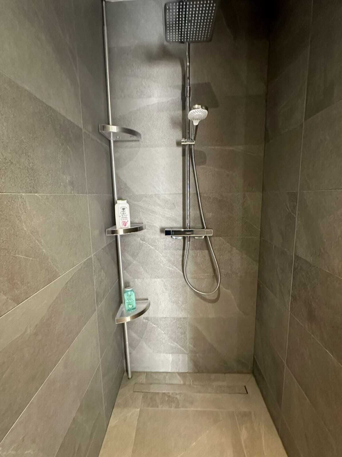 Eine Dusche mit Duschbrause, Wandarmatur und Ablage für Toilettenartikel.