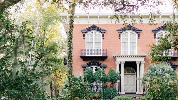A brick building with a central entrance, surrounded by lush greenery and trees. - Historic District, Walkable w/Free Parking & Patio (Savannah)
