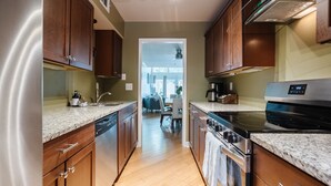 A modern kitchen with wooden cabinets, granite countertops, stainless steel appliances, and a view into the dining area. - Historic District, Walkable w/Free Parking & Patio (Savannah)