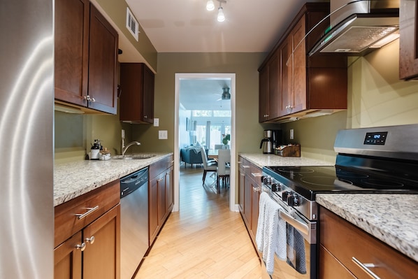 A modern kitchen with wooden cabinets, granite countertops, stainless steel appliances, and a view into the dining area. - Historic District, Walkable w/Free Parking & Patio (Savannah)