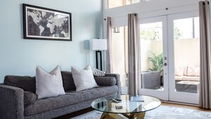 A modern living room with a grey sofa, a glass coffee table, and a world map artwork on the wall. - Historic District, Walkable w/Free Parking & Patio (Savannah)