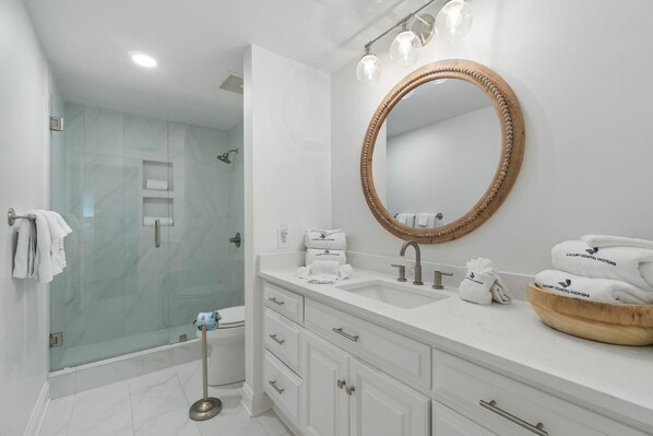 Une salle de bain moderne dotée d’une douche à parois de verre, d’un grand miroir, de meubles blancs et d’un meuble-lavabo avec un lavabo en forme de coupe.