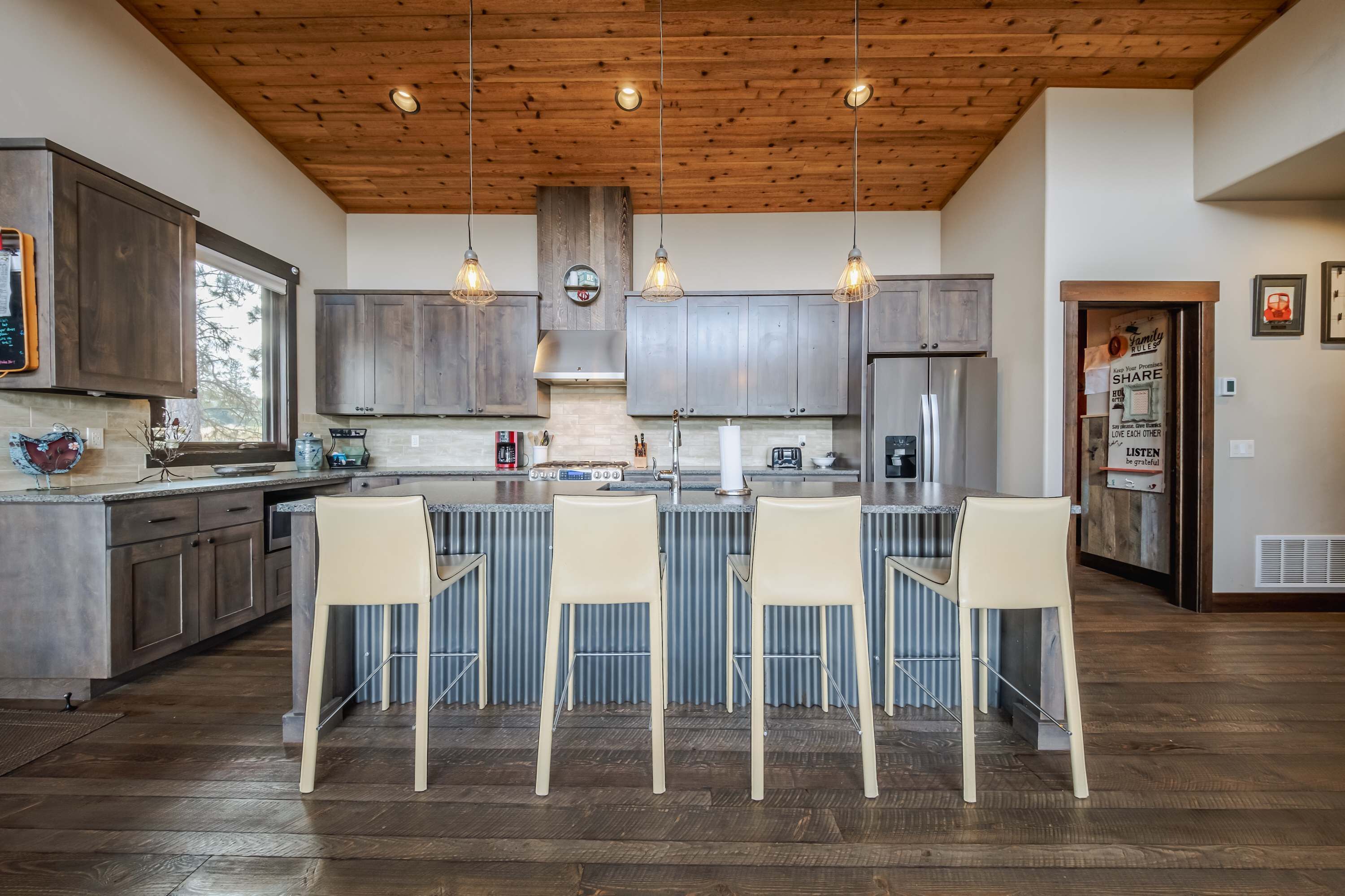A modern kitchen with wooden ceiling, stainless steel appliances, and a central island with bar stools.