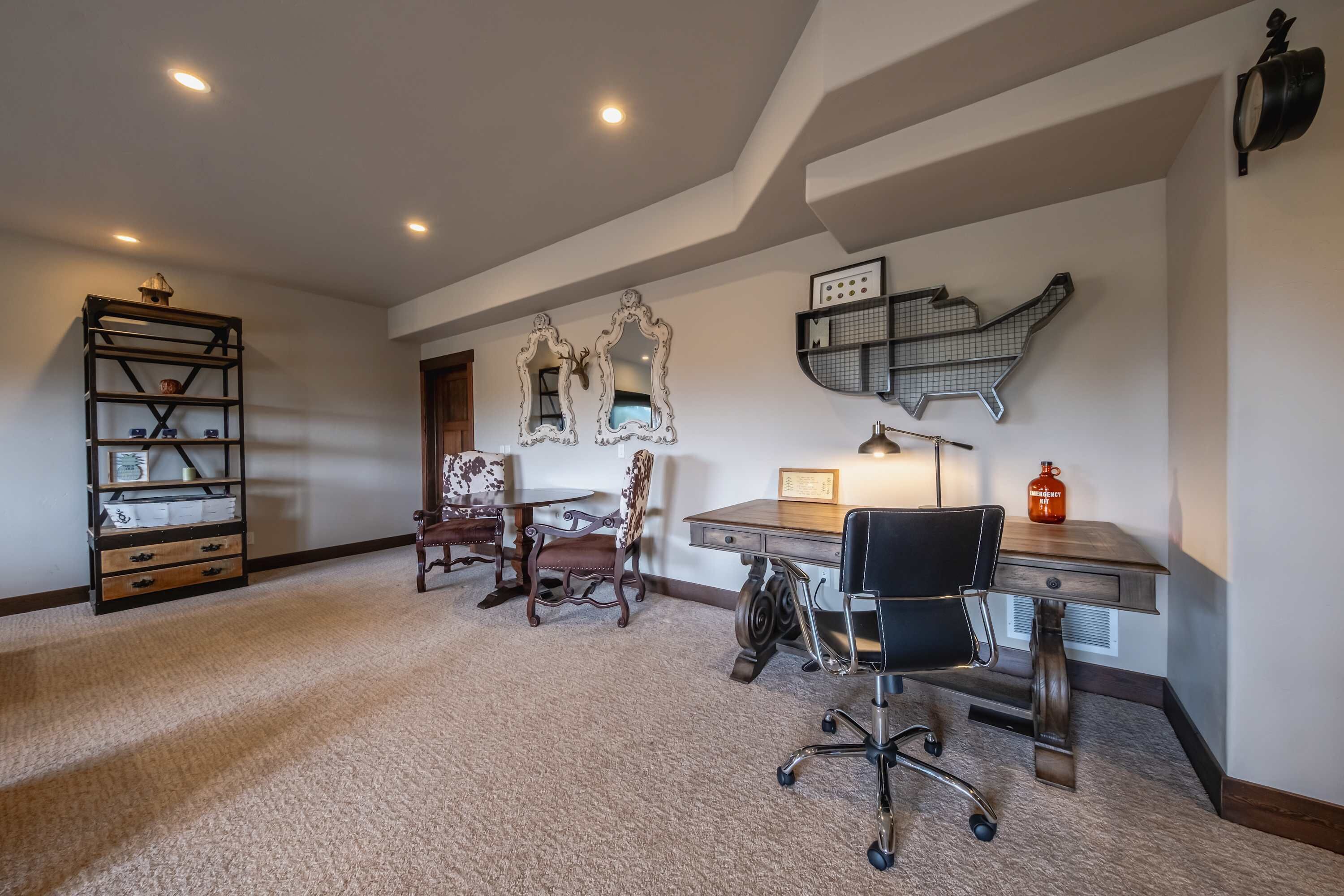 A spacious room with a large desk, two chairs, a bookshelf, and decorative mirrors.