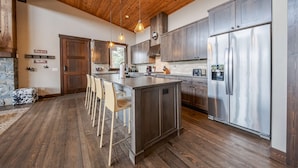 A modern kitchen with wooden flooring, a central island with bar stools, stainless steel appliances, and a stone fireplace. - Treehouse at the Wilderness Club (Eureka)