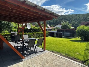 Una veranda coperta con una griglia, posti a sedere all'aperto e vista su un prato verde e delle colline.