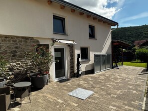 Un edificio con fachada de piedra, un patio cubierto con mobiliario exterior y una puerta que da a un espacio interior.