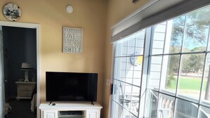 A living room with a TV on a white cabinet, a blue sofa, and a large sliding glass door leading to an outdoor area. - 2 BR 2 BA Royal Poste condo in Sea Trail Resort Sunset Beach, NC (Sunset Beach)