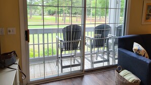 A room with a sliding glass door leading to an outdoor deck with two chairs and a view of a grassy area with trees. - 2 BR 2 BA Royal Poste condo in Sea Trail Resort Sunset Beach, NC (Sunset Beach)