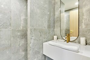 Een badkamer met een witte wastafel, een gouden kraan en marmeren wanden.