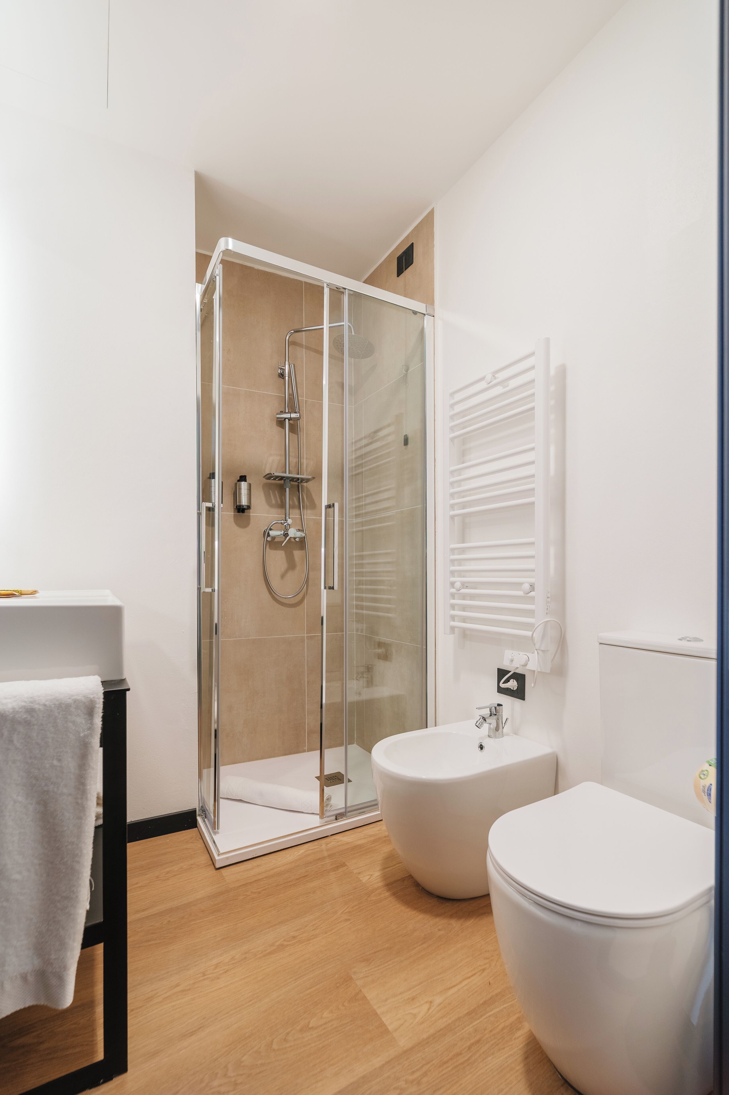 Un baño moderno con ducha de vidrio, lavamanos blanco y dos inodoros.