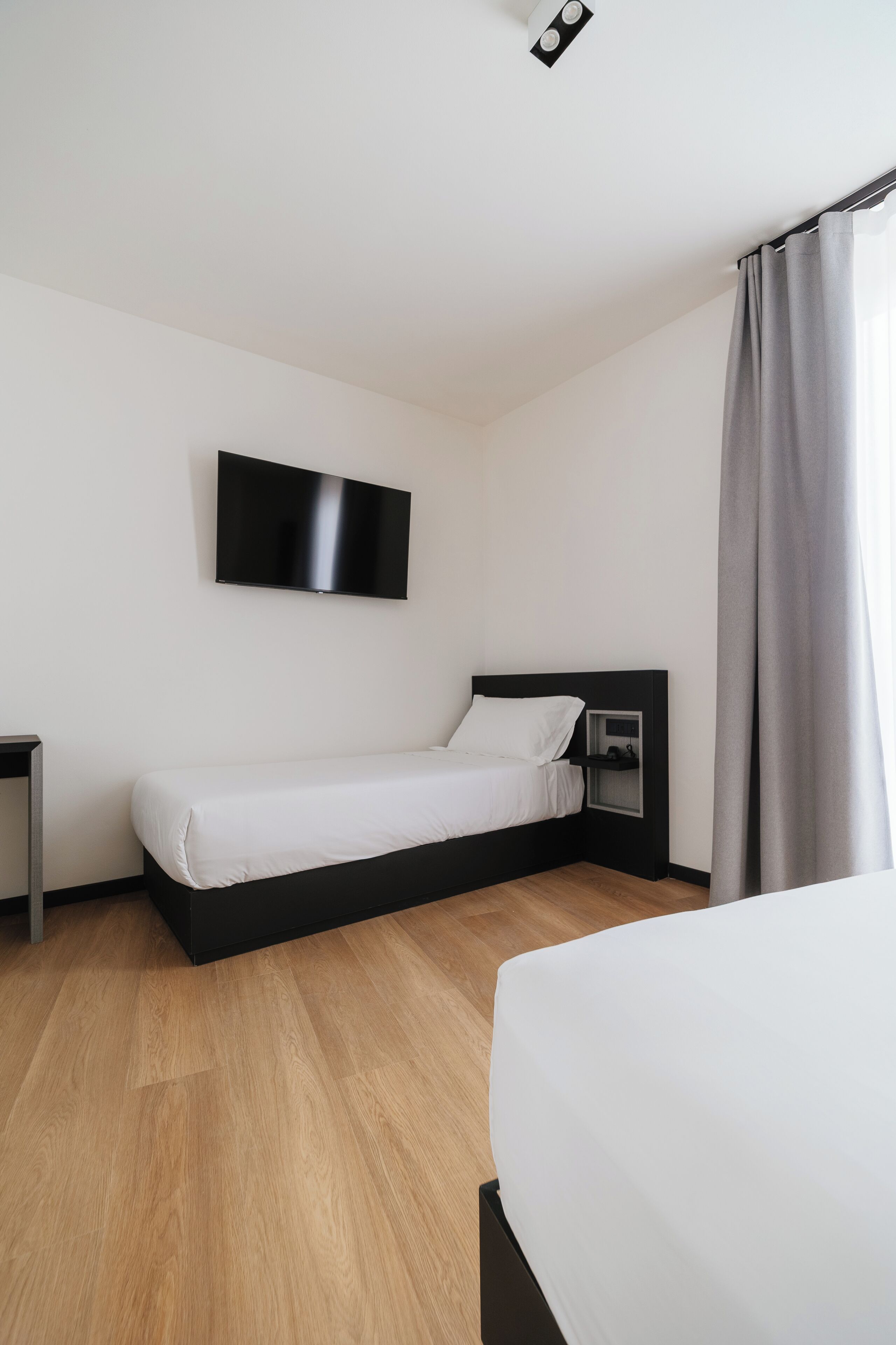 A modern hotel room with a single bed, a TV mounted on the wall, and a wooden floor.