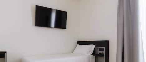 A modern hotel room with a single bed, a TV mounted on the wall, and a wooden floor.