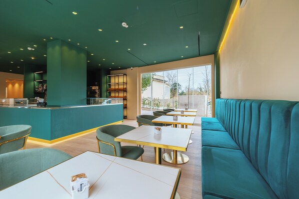 A modern restaurant interior with teal-colored seating, a bar area, and large windows providing natural light. - Aspio Hotel (Camerano)