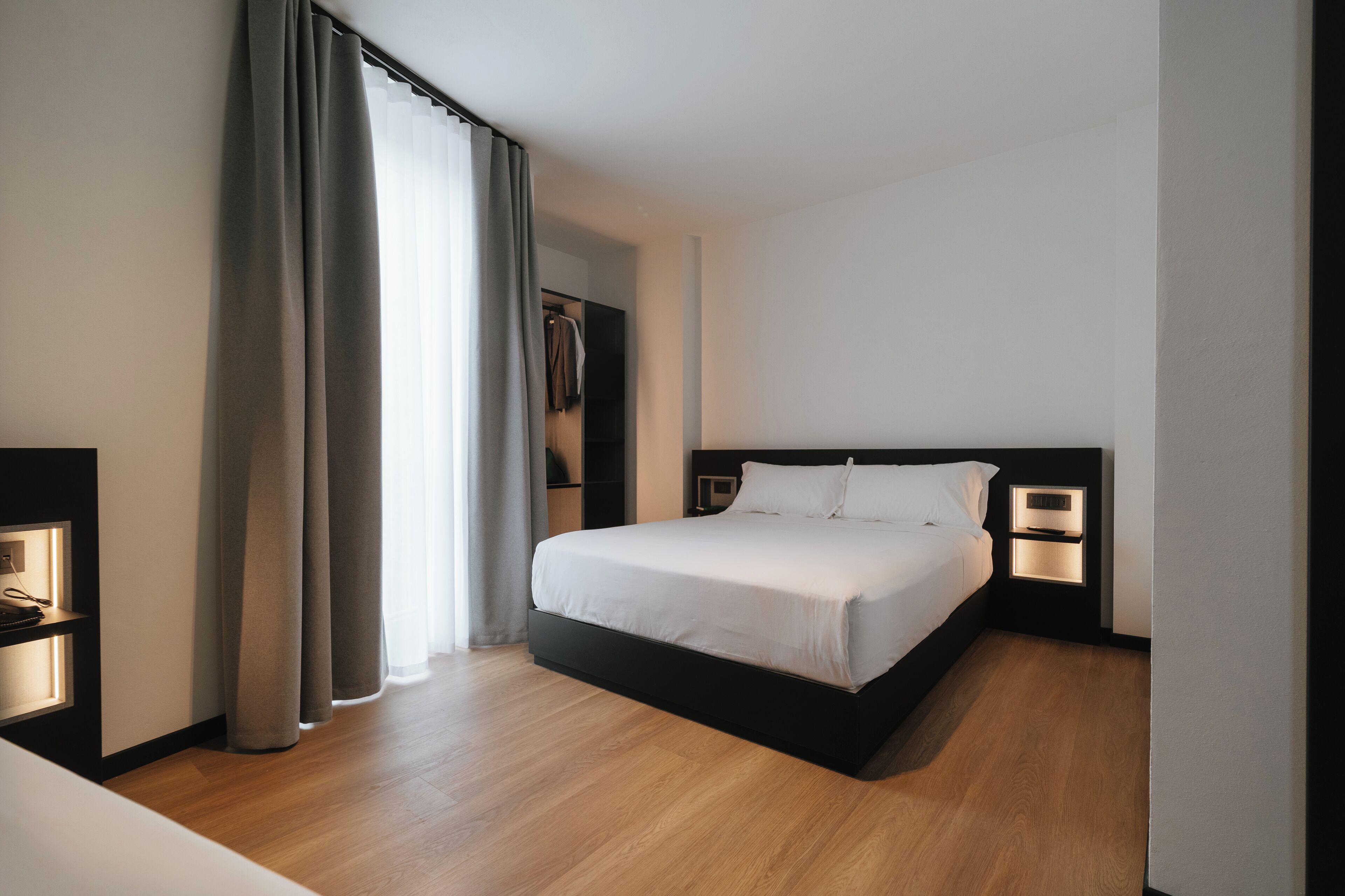 A modern hotel room with a large bed, bedside lamps, a wardrobe, and a view of the outdoors.