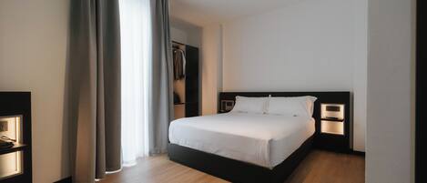 A modern hotel room with a large bed, bedside lamps, a wardrobe, and a view of the outdoors.