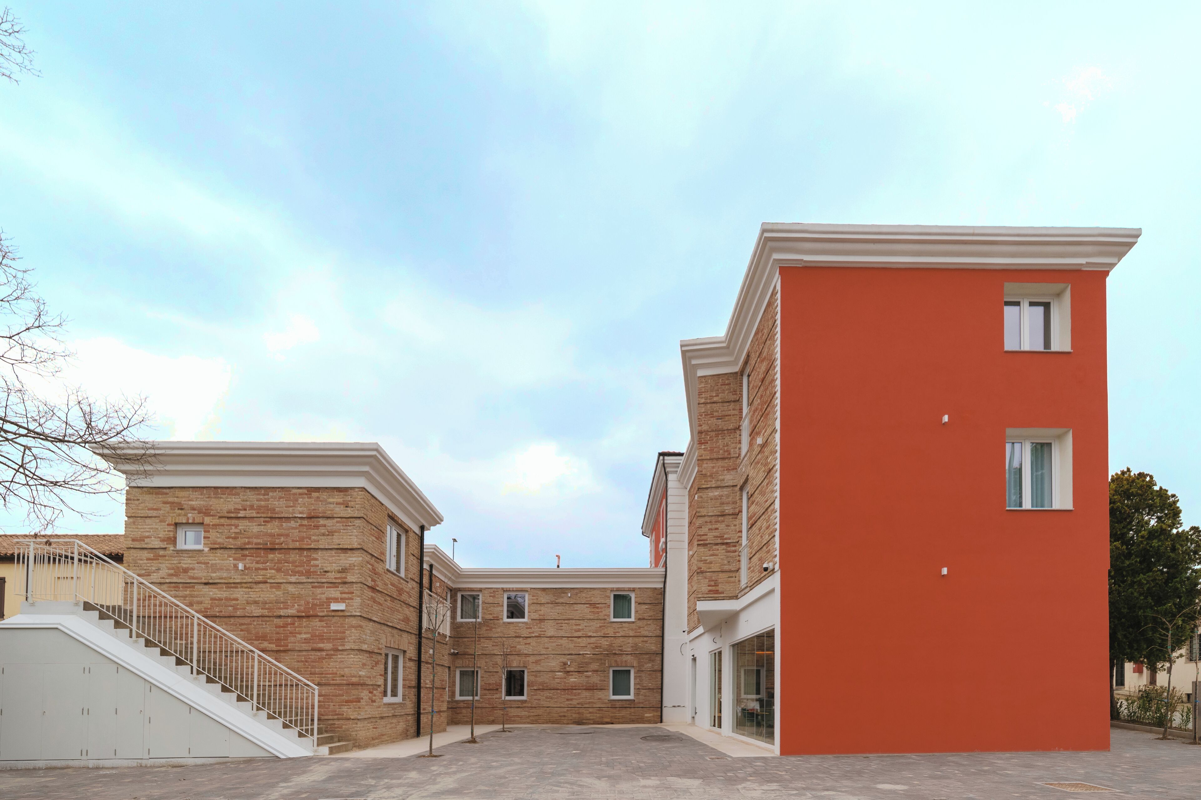 A multi-story building with a brick facade and a red section, featuring a staircase and a small window.