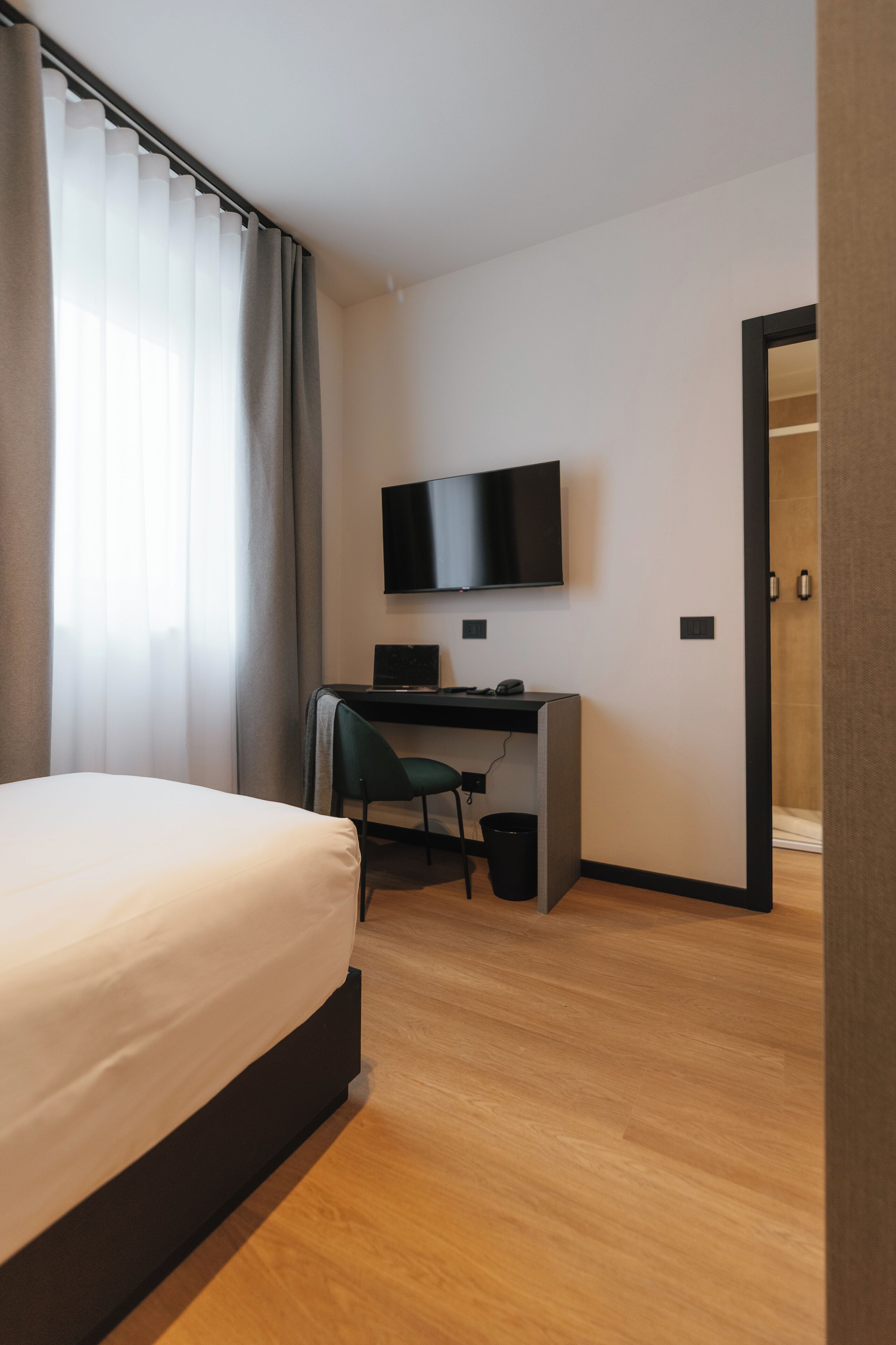 Habitación de hotel con cama, escritorio con computadora, televisión y puerta que da a otra habitación.