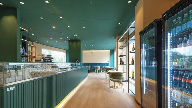 Un espace bar moderne doté d’un long comptoir, de sièges et d’un grand réfrigérateur rempli de boissons.