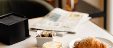 Una mesa con un croissant, una taza de café y un periódico.