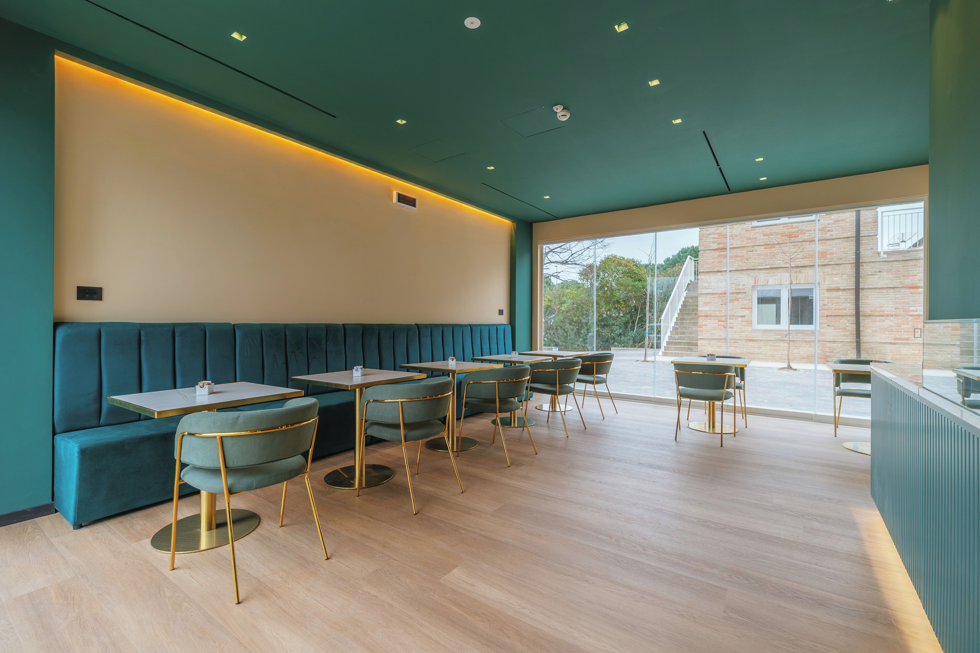 A modern restaurant interior with teal-colored booths, round tables, and green chairs.