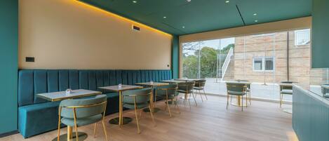 A modern restaurant interior with teal-colored booths, round tables, and green chairs.