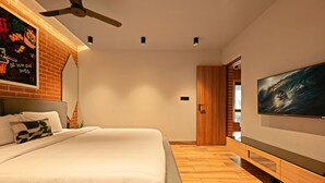 A modern bedroom with a large bed, a ceiling fan, a TV, and a brick wall with graffiti. - Charming 1-bedroom apartment in delightful Arpora with WiFi, AC, fitness room (Arpora)