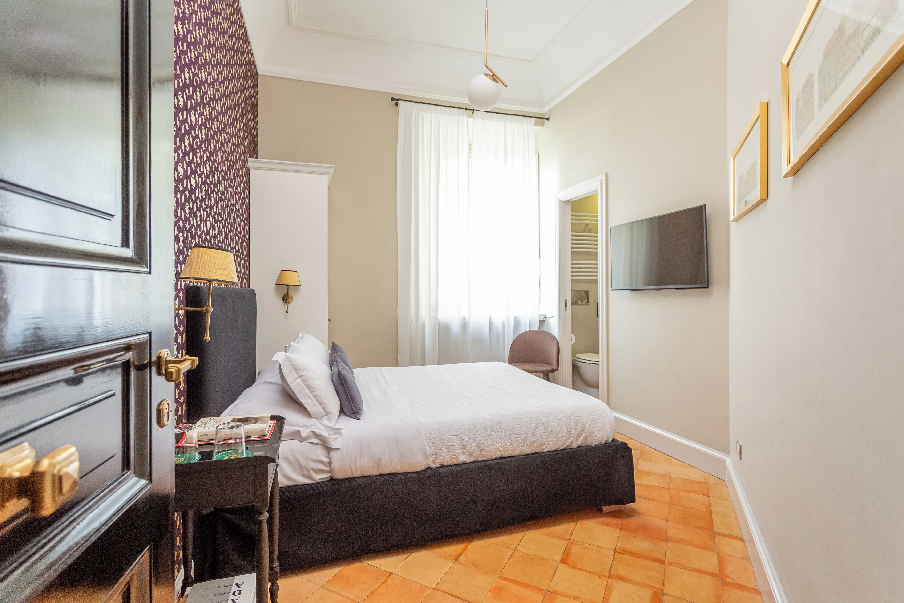 Una habitación de hotel con una cama, mesita de noche, lámpara y televisor en la pared.