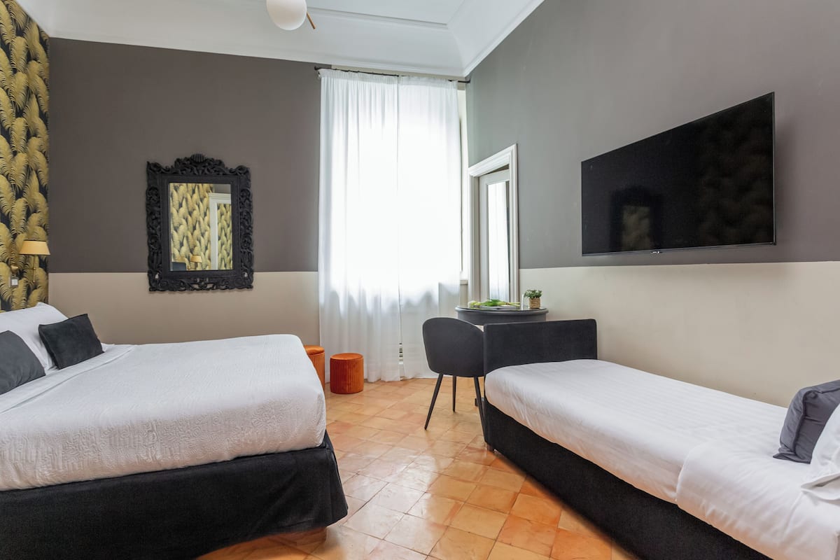 A hotel room with two beds, a desk, a chair, a mirror, and a television.