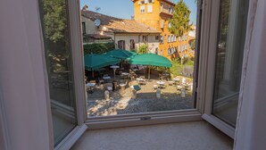 A view through a window of a courtyard with outdoor seating, a building with a tiled roof, and a clear sky. - Hotel Parrasio (Rome)
