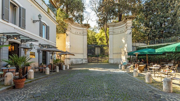 A cobblestone courtyard with outdoor seating, a building entrance, and a gate. - Hotel Parrasio (Rome)