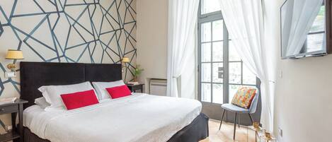 Una habitación de hotel moderna con una cama grande, un muro con patrón geométrico, una ventana con cortinas translúcidas y un televisor de pantalla plana montado en la pared.