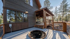 A wooden deck with a hot tub, a covered seating area, and a large window overlooking a forest. - Wilderness Club Cabin Sleeps 7 (Eureka)