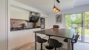 Une cuisine moderne dotée d’un îlot central, d’appareils électroménagers en acier inoxydable et de luminaires suspendus.