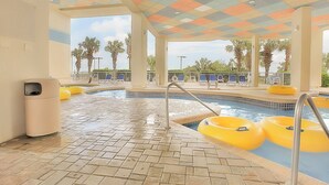 A pool area with a tiled floor, a pool, yellow floating rings, and lounge chairs.