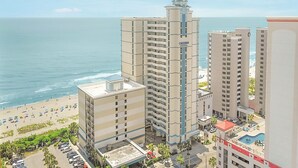 A high-rise hotel with multiple floors, a central tower, and a beach view.
