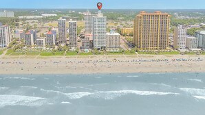 A coastal cityscape with high-rise buildings, a beach, and a red location marker.