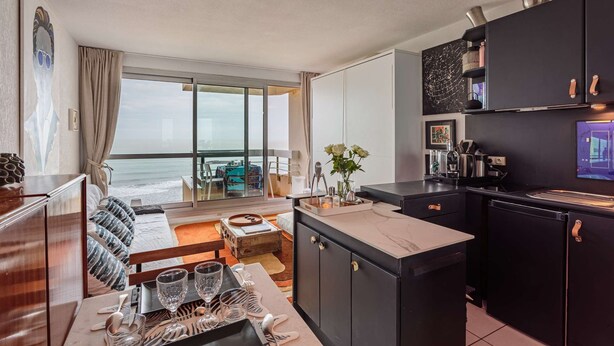 A modern kitchen with a large island, a dining area with a view of the ocean, and a cozy seating area with a sofa and cushions. - - (BIARRITZ)