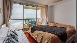 A hotel room with a bed, a sofa, a large window with a view of the beach and ocean, and a sliding door leading to a balcony. - - (BIARRITZ)