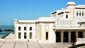 Un grand bâtiment blanc, sur lequel on peut lire l’inscription « CASINO », doté d’une entrée imposante et offrant une vue sur la mer.