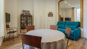 Un coin repas comprenant une table ronde, quatre chaises, un canapé de couleur turquoise, un grand miroir et un meuble avec des portes en verre.