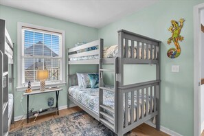 A bunk bed with a window, a desk with a lamp, and a decorative wall piece. - New for 2026 - single family 3BR/2BA plus bonus with private pool and hot tub! (Carolina Beach)