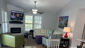 Un salon spacieux doté d’un grand téléviseur, d’un ventilateur de plafond et d’un coin repas avec un banc et une table.